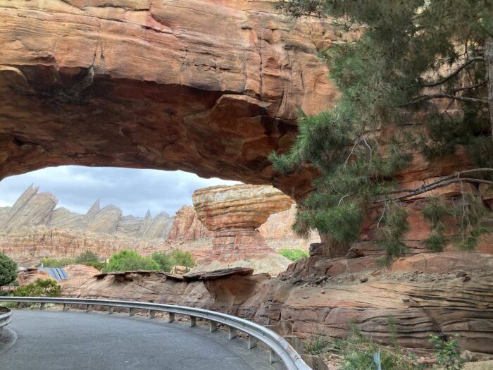 Photo taken on pathway between San Fransokyo Square and Cars Land in Disney California Adventure Park. Shows rock work, asphalt, railing and foliage around Radiator Springs Racers in Disneyland Resort.
