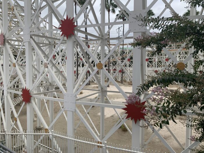 View of the supports under the Incredicoaster attraction at Disney California Adventure Park at Disneyland Resort. The photo shows read, white and gold structures beside greens an oink foliage.