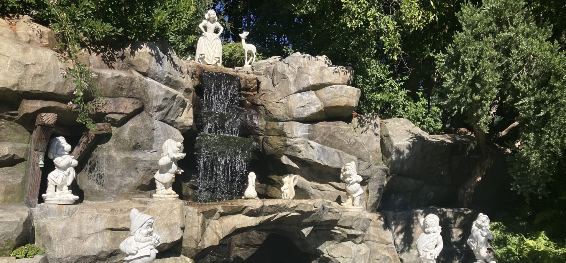 Snow White and the Svene Dwarves around a waterfall east of Sleeping Beauty Castle at Disneyland Park.