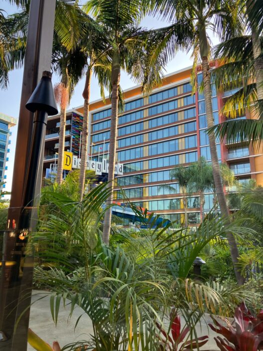Photo of Disneyland Hotel showing guest room tower behind palm trees and other landscaping. Also visible in the photo is the “Disneyland” sign atop the monorail themed waterslides in the hotel pool.