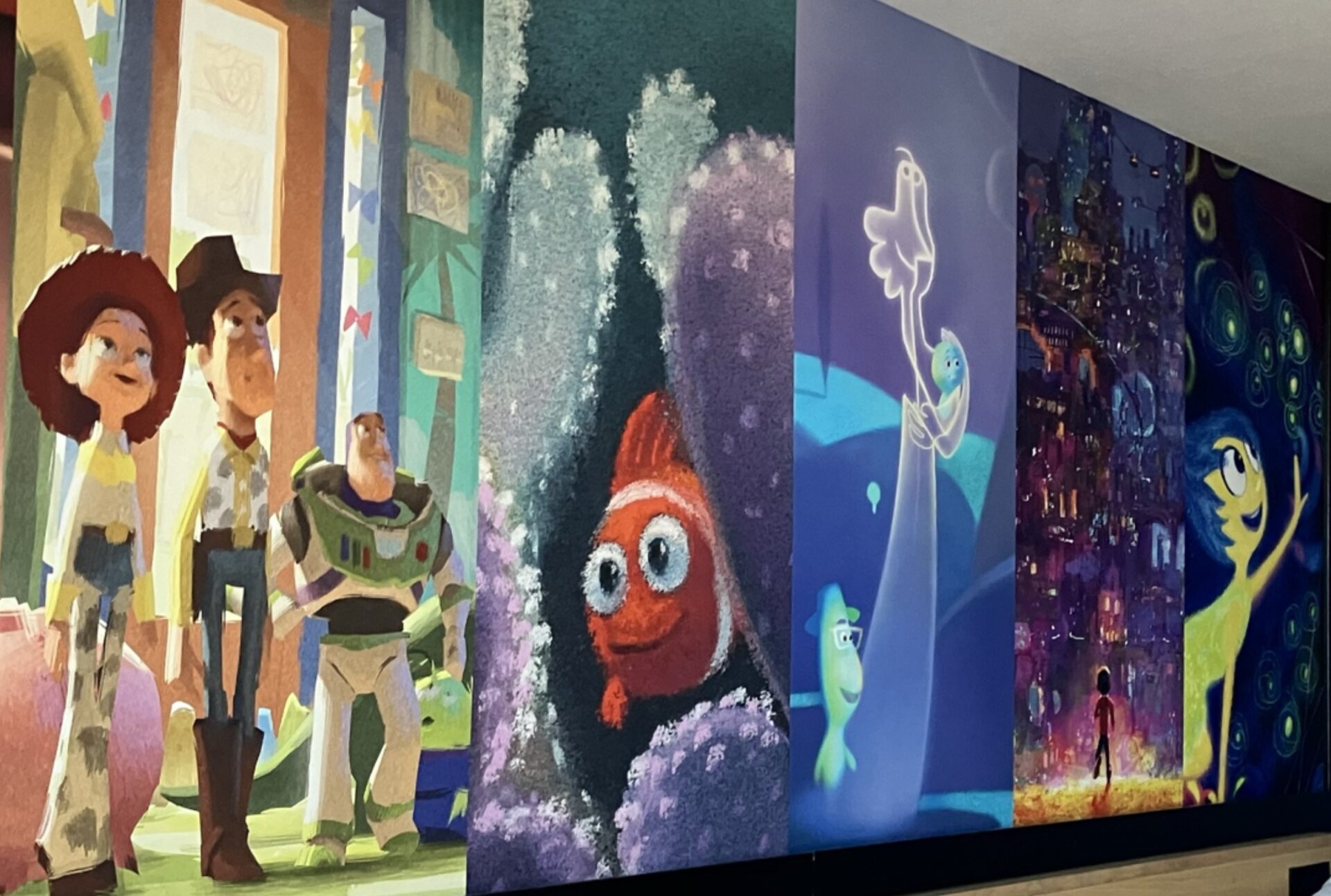 Ombré mural in guest room at Pixar Place Hotel at Disneyland Resort in Anaheim, California. Photo shows mural of Jessie, Woody and Buzz from Toy Story and scenes from Finding Nemo, Soul, Coco and Inside Out. Mural moves from warm to cool tones.