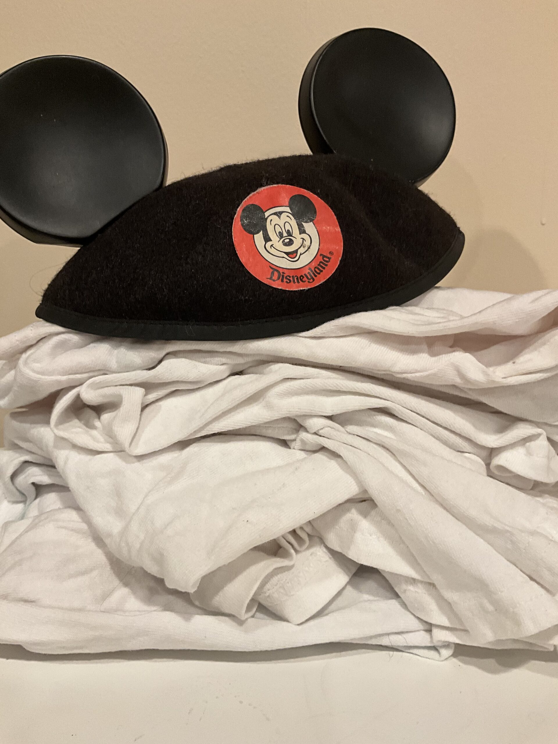 Disneyland Mickey Mouse Club ears on top of a pile of laundry to illustrate an article with advice for doing laundry at Disneyland.