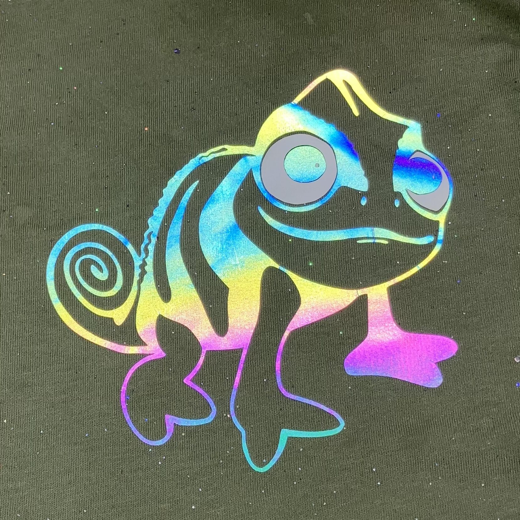 Photo of Pascal from Tangled in iron-on rainbow reflective vinyl on a kids t-shirt. Illustrates that basic functional clothing can be enhanced for a trip to Disneyland.