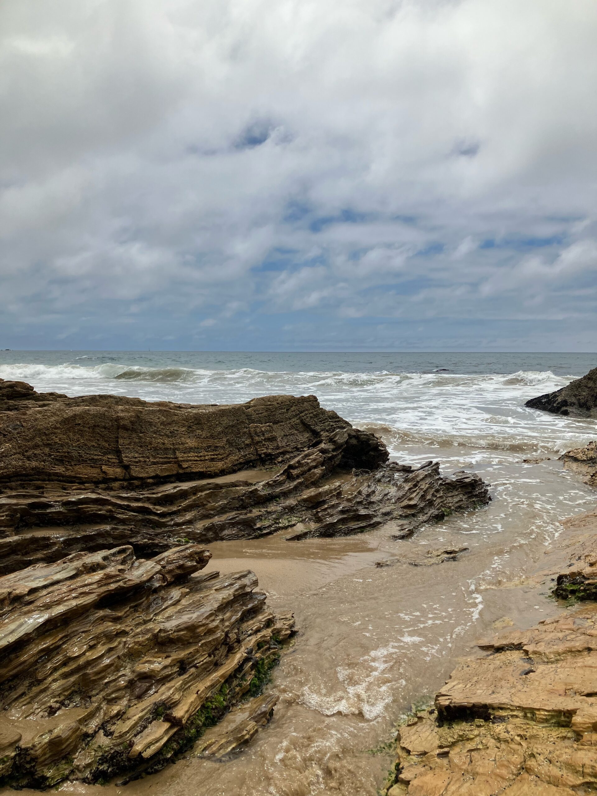 View from the beach at Crystal Cove State Park with water rushing between tan rocks and over sand. A good way to spend a rest day in between park visits at Disneyland Resort.