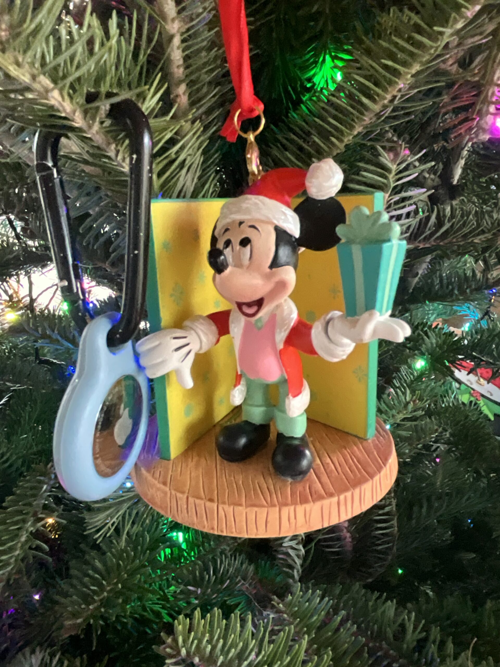 Mickey ornament next to Apple AirTag on a keychain clip. Illustrates that AirTags are useful in Disney parks and on sale for the holidays.