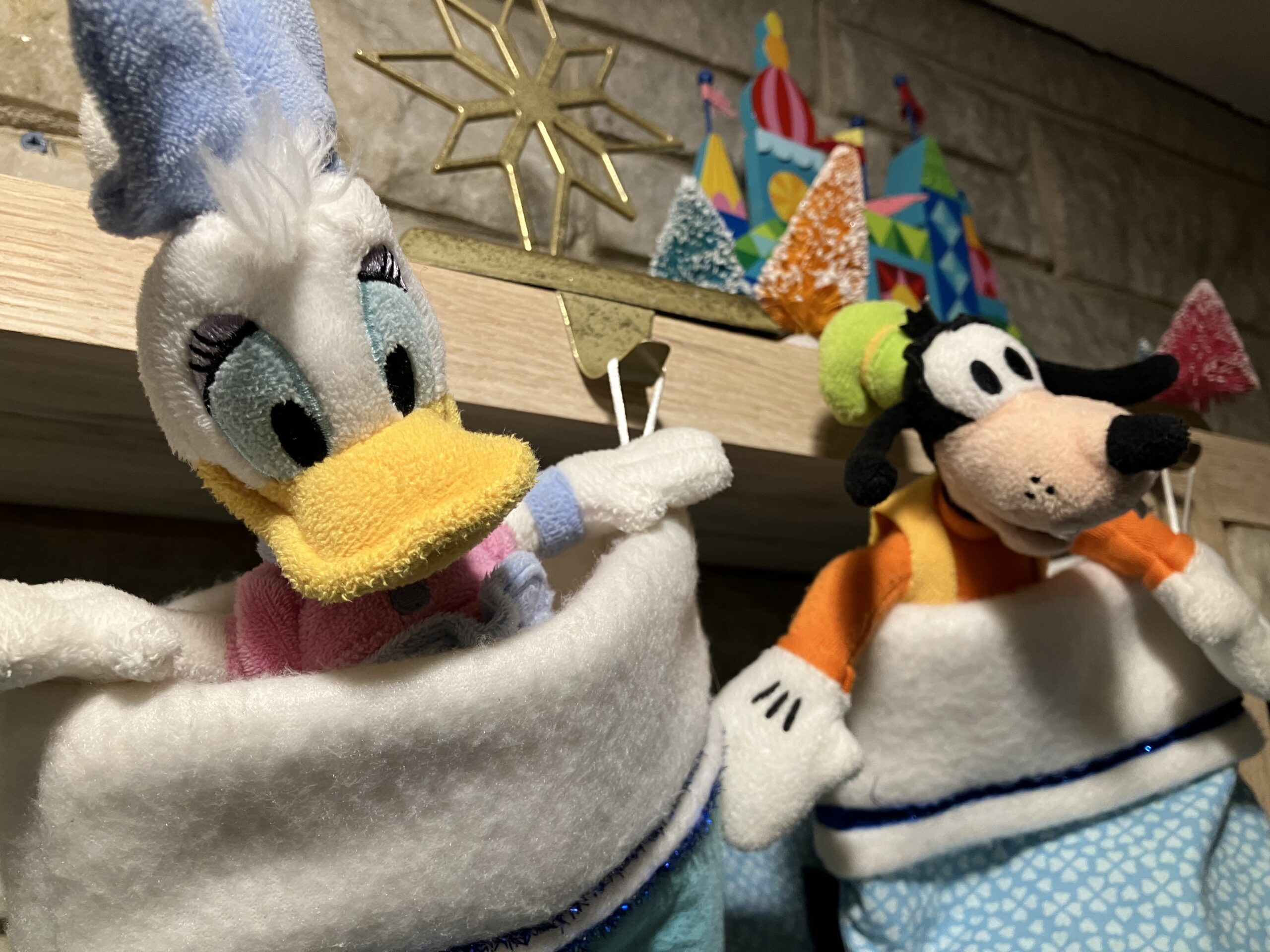 Daisy and Goofy plush in stockings hanging from mantle showing two Disney themed stocking stuffers for Christmas.