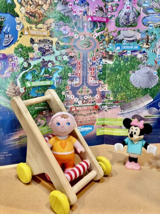 Toy figures in toy stroller in front of map of Disneyland Park with Minnie Mouse figure.