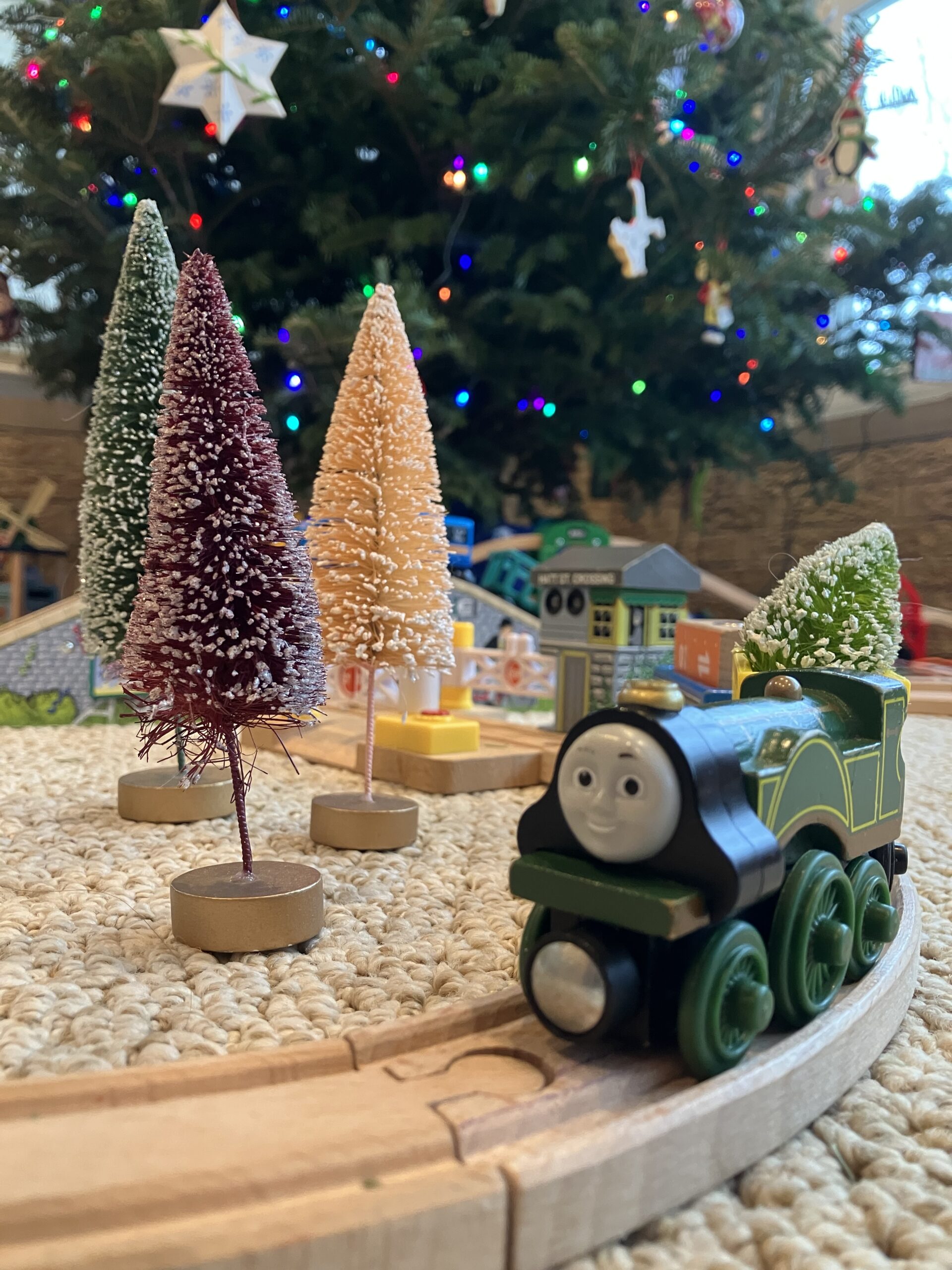 Emily train from Thomas the Tank Engine next to battle brush trees and Christmas tree showing the family tradition of putting a wooden railway around a Christmas tree.