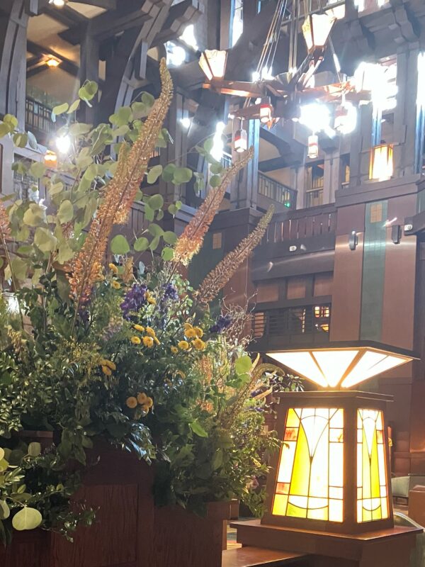 Photo of lobby of Grand Californian Hotel and Spa in Disneyland Resort. Phot shows Arts and Crafts style light fixtures and a large flower arrangement.