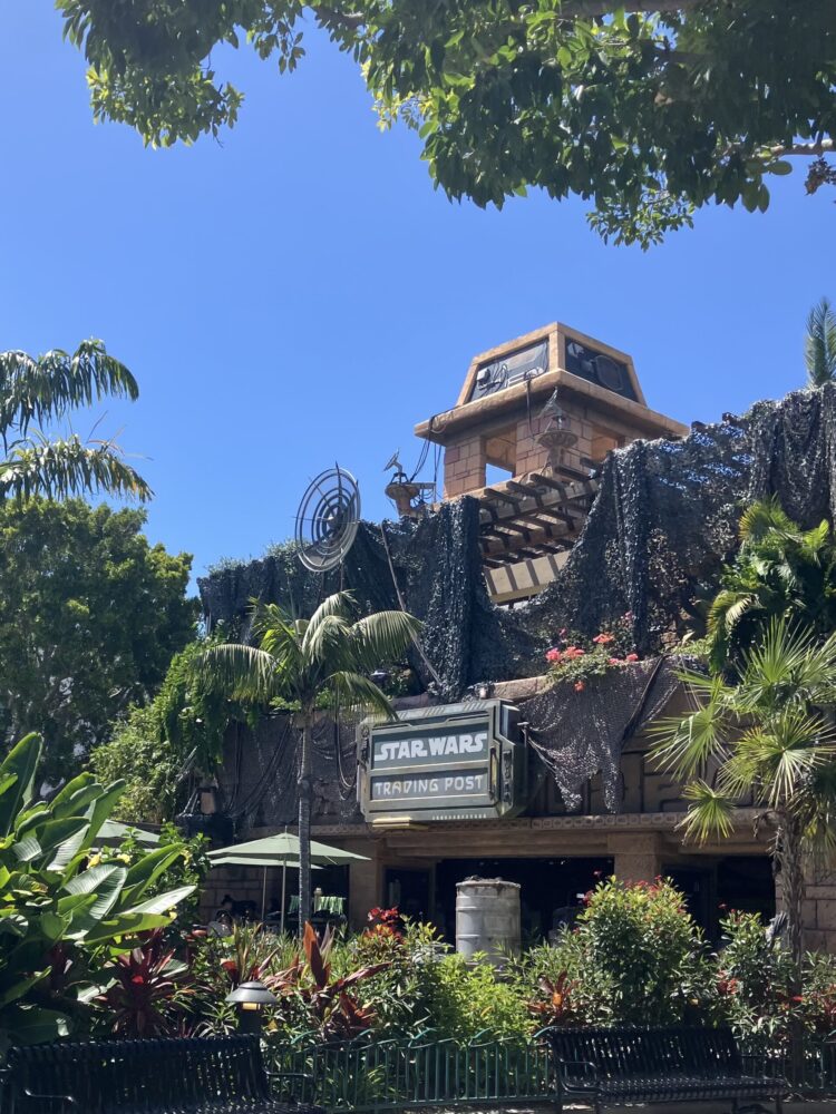 Photo of Star Wars Trading Post at Downtown Disney District in Disneyland Resort. Shows lots of foliage around tan store.